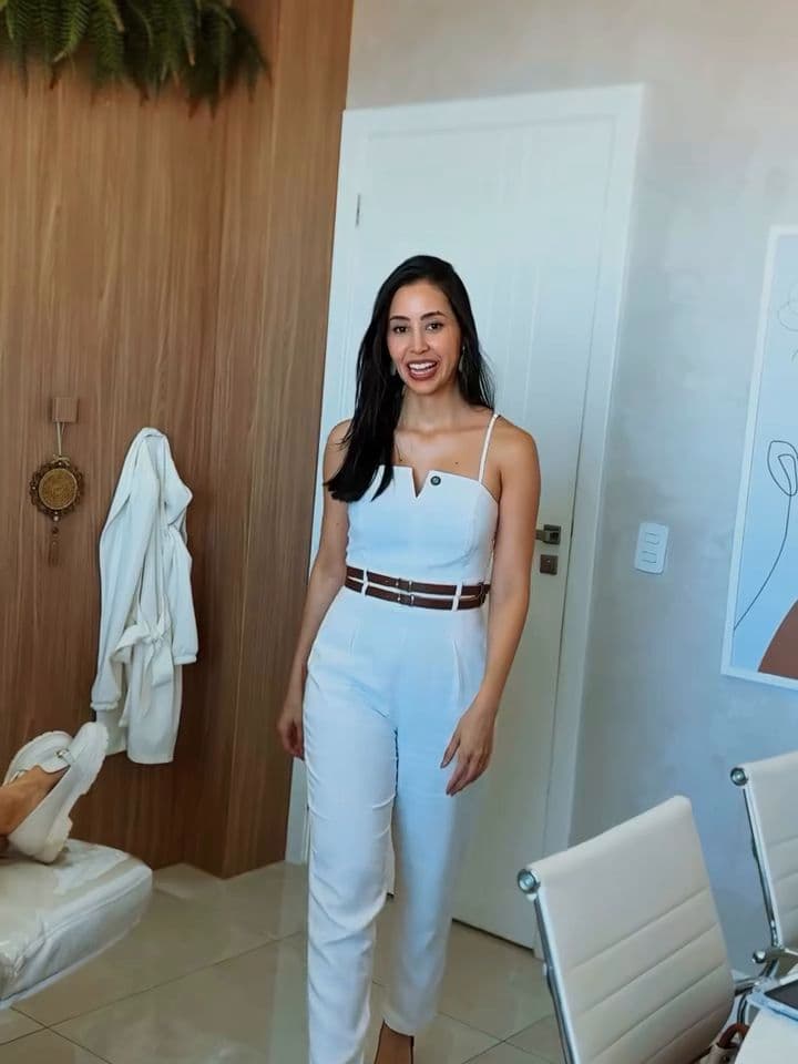 Juliane entrando na sala de procedimentos, com o ripado de madeira, as cadeiras brancas e o jaleco pendurado